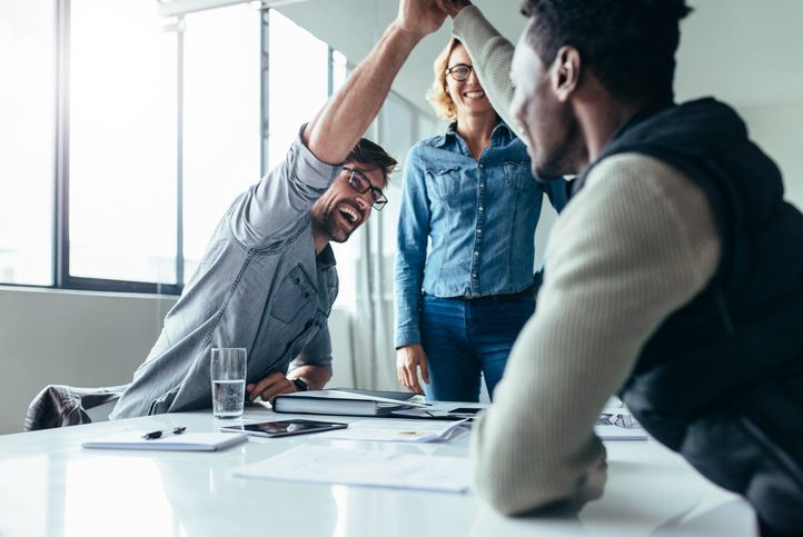 Two colleagues giving high five in meeting. Business people celebrating success in conference room.