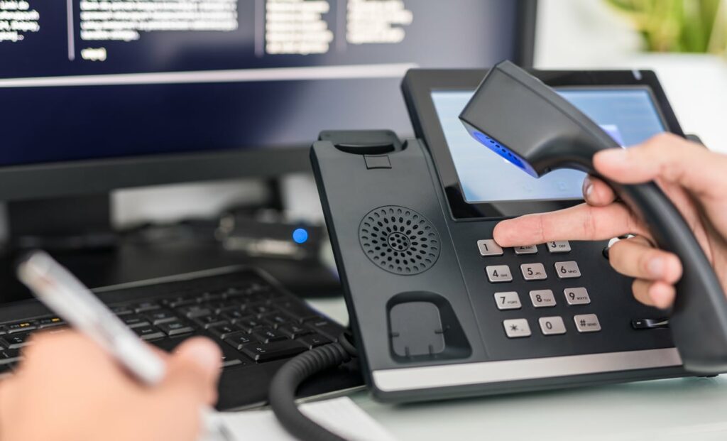 hand-holding-corded-phone-while-dialing-number-at-work-station-desk